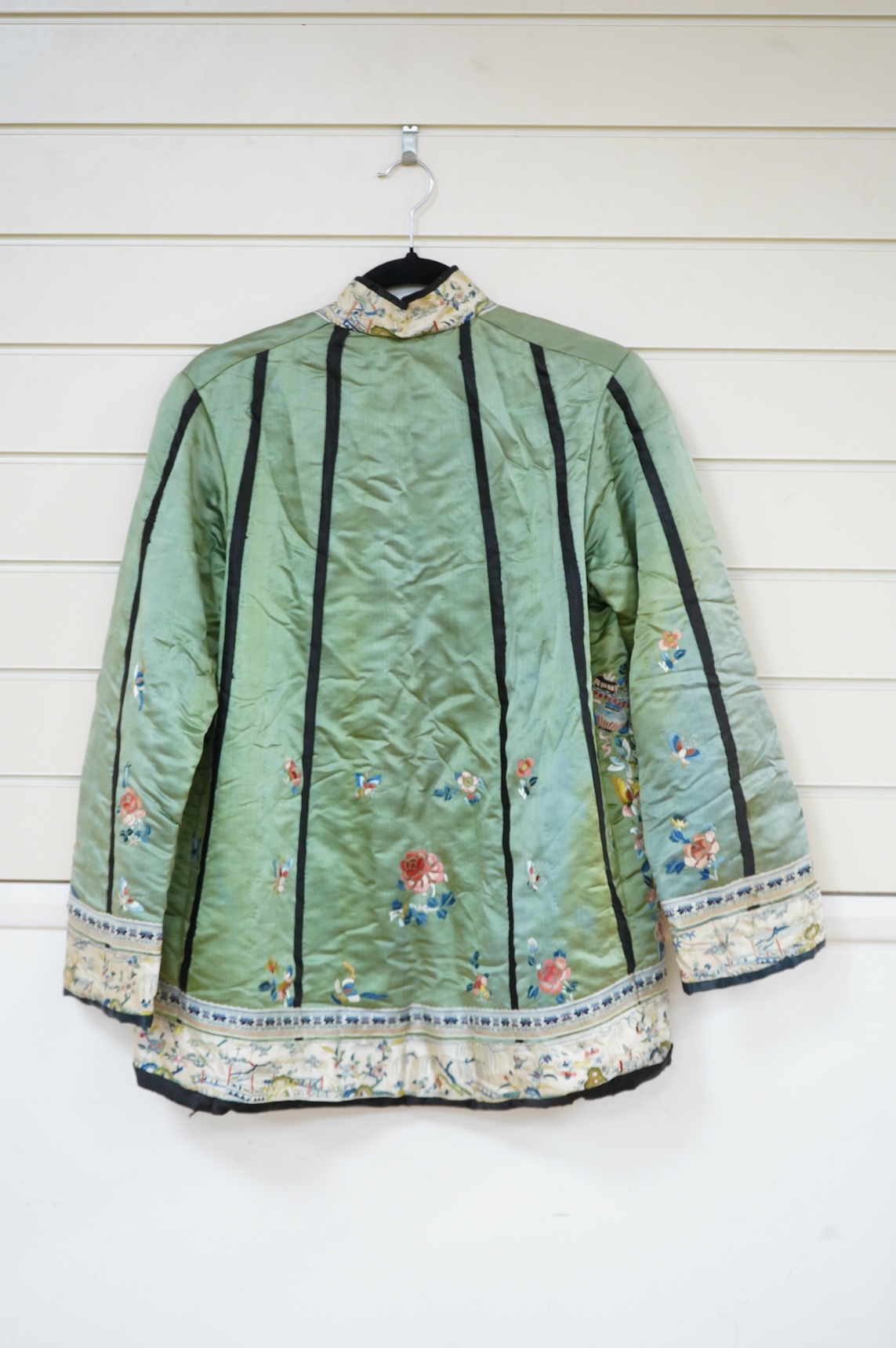 An early 20th century Chinese green silk polychrome embroidered jacket. Worked with Chinese knot embroidery and stem stitch into flowers, butterflies and bats, edged with woven silk ribbon and a figurative embroidered bo